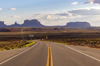 Open road view towards iconic Monument Valley rock formations at sunset.