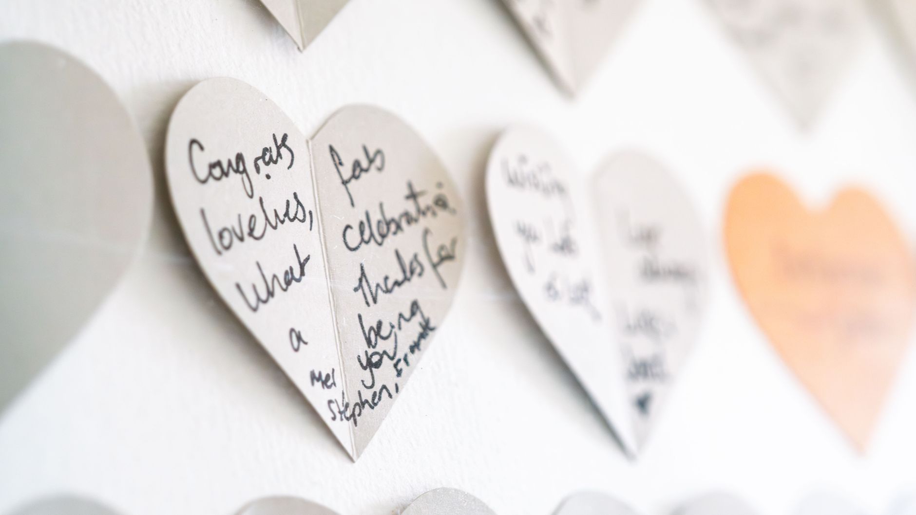 Close-up view of heart-shaped cards with handwritten congratulatory messages on a wall.