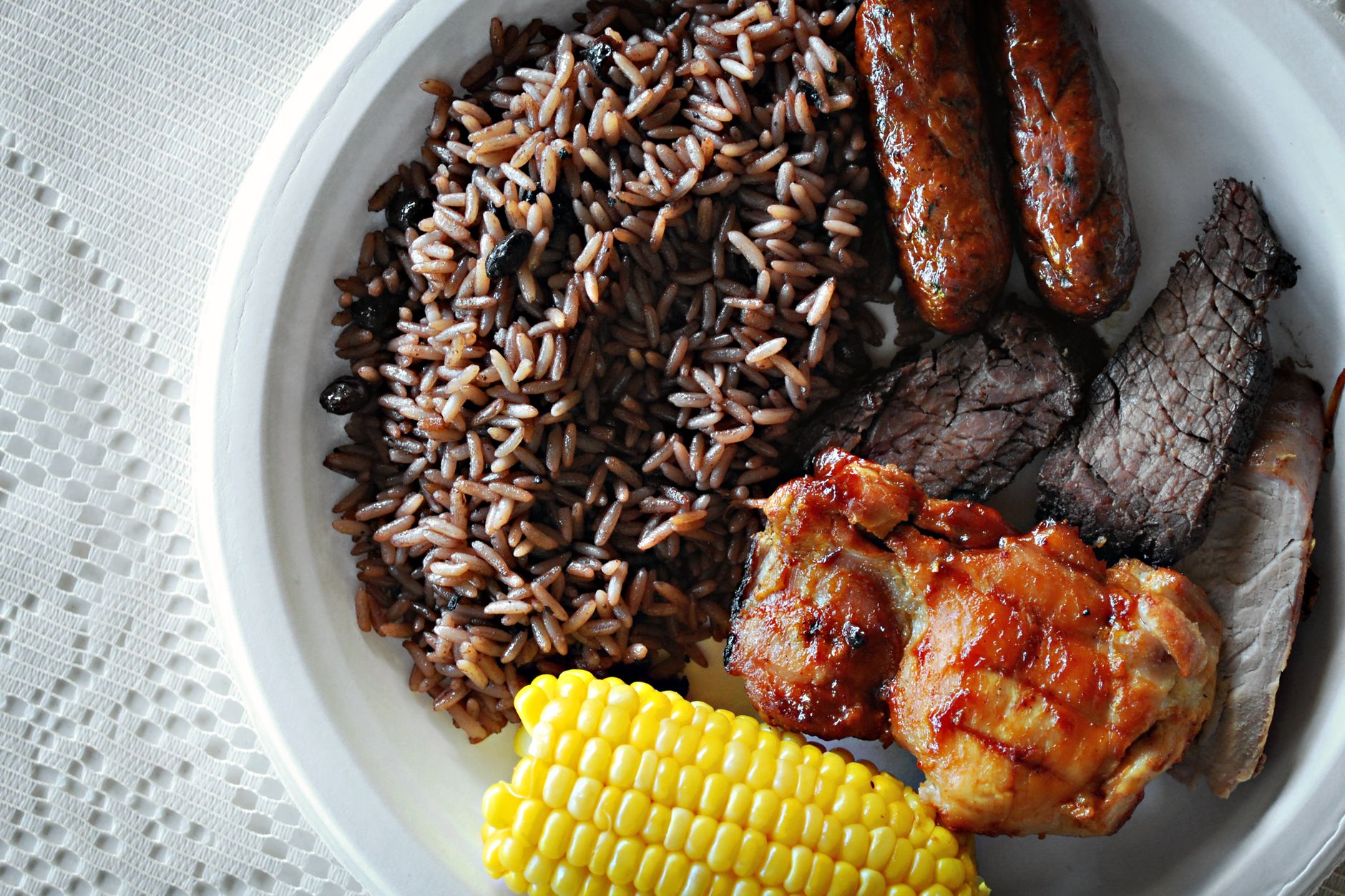 A hearty meal featuring rice, grilled meats, and corn on a plate.