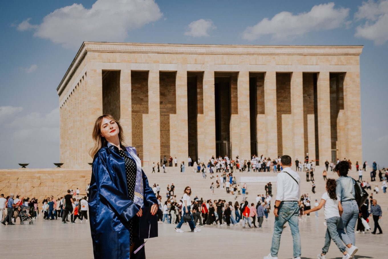 Graduate celebrating at Anıtkabir amid a bustling crowd during the day.