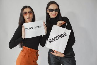 Two stylish women holding Black Friday shopping bags and signs, ready for deals.