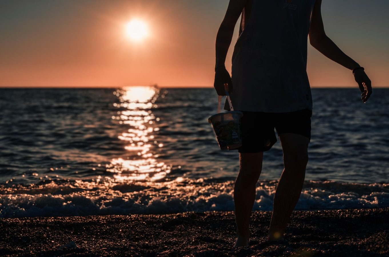 A person walks along the beach at sunset in Türkiye, casting a silhouette against the sea.