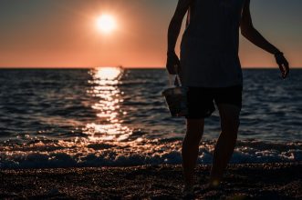 A person walks along the beach at sunset in Türkiye, casting a silhouette against the sea.