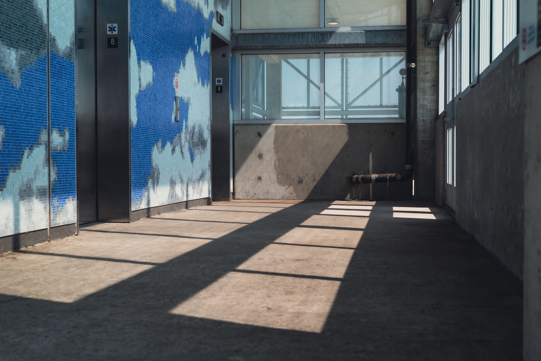 A contemporary interior with blue mosaic walls and sunlight casting shadows through windows.