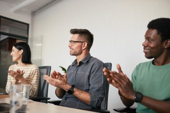 A diverse group of coworkers applauding during an office meeting, showcasing teamwork and support.