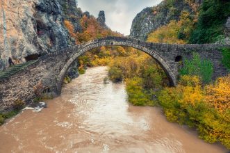 Stunning view of an old stone bridge over a river in Pindus National Park, Greece, during fall.