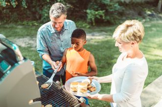 Family enjoying a BBQ in the backyard grilling burgers on a sunny day.
