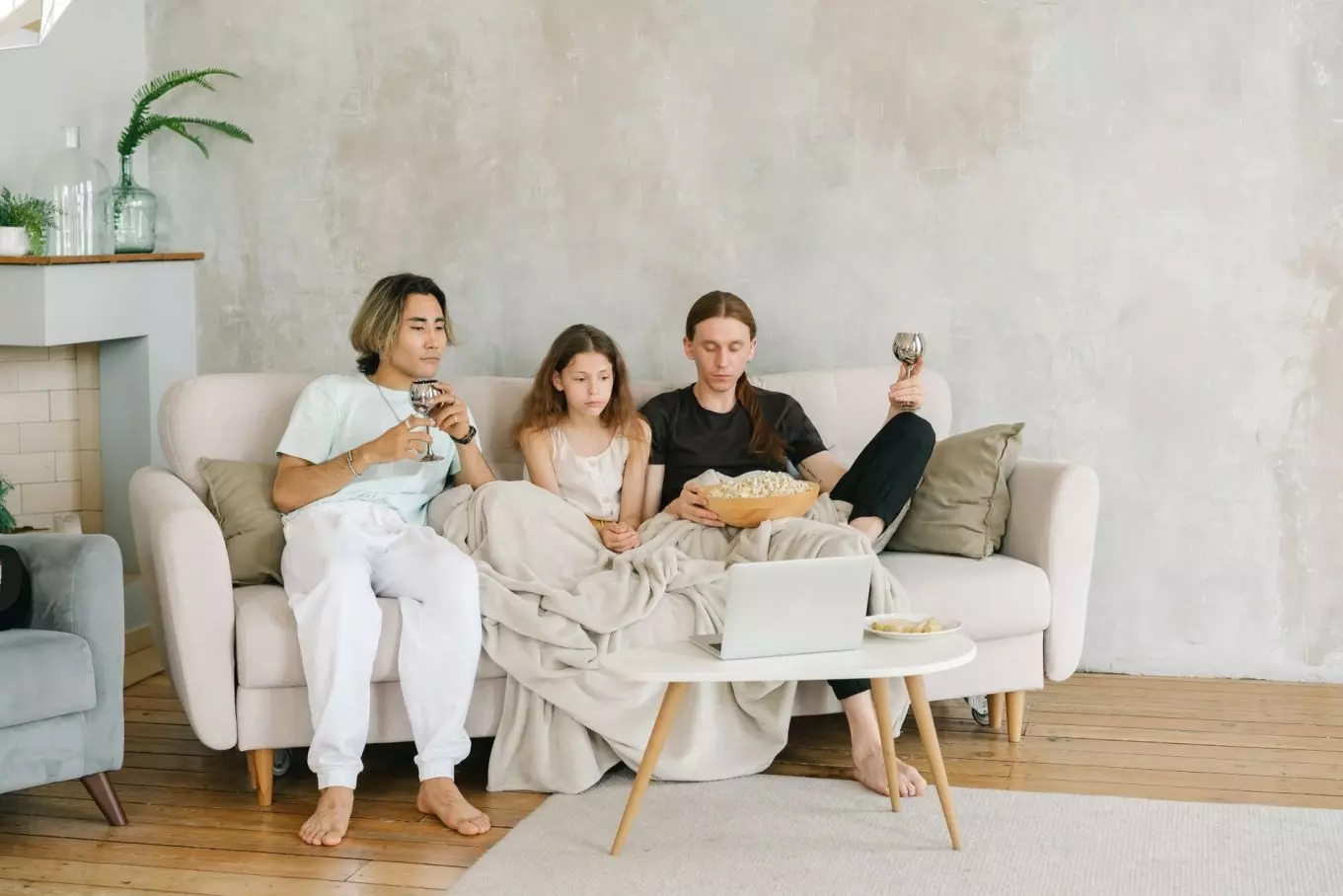 Three young friends enjoying a movie night on the sofa with popcorn and drinks.