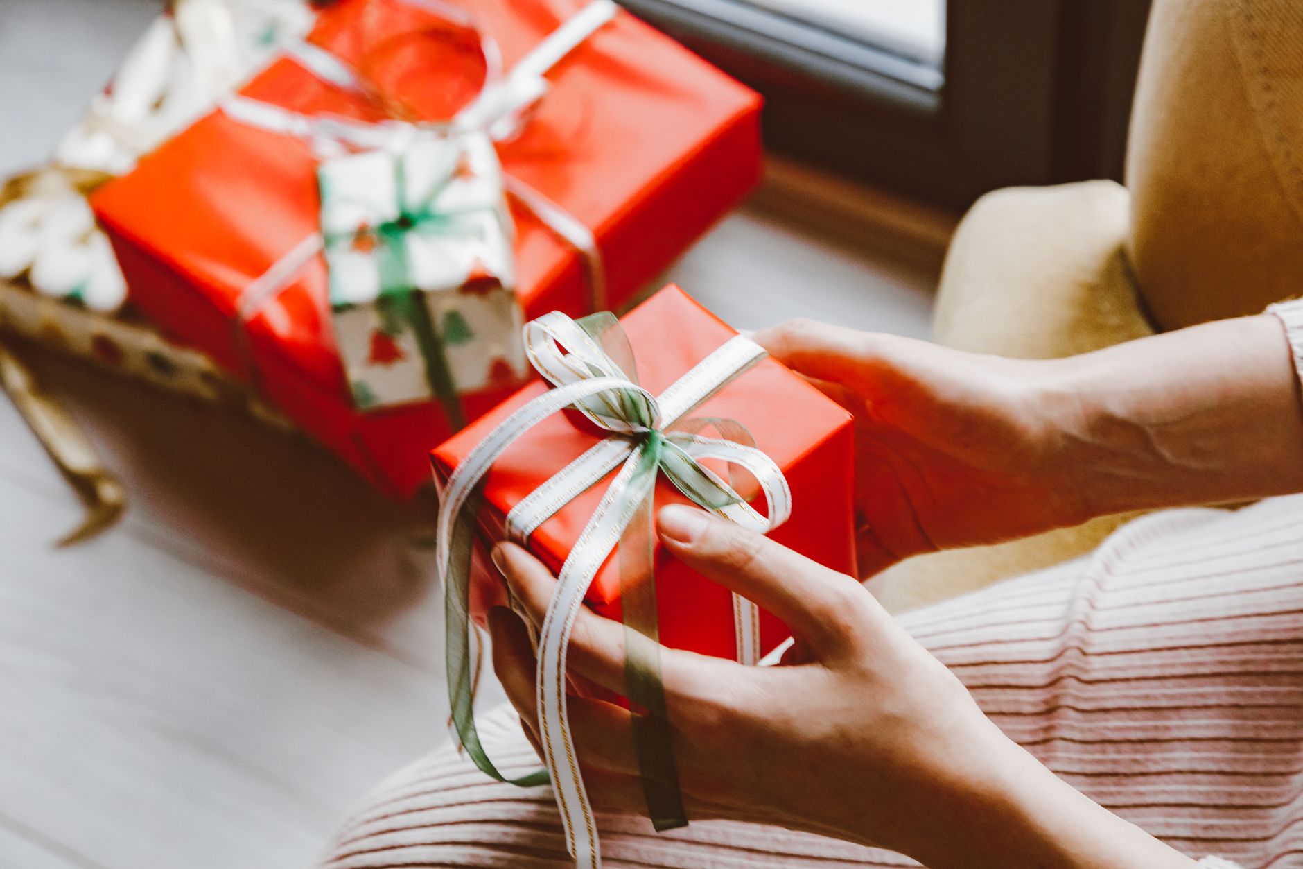 Close-up of hands holding a wrapped Christmas gift tied with ribbon, capturing the festive mood.