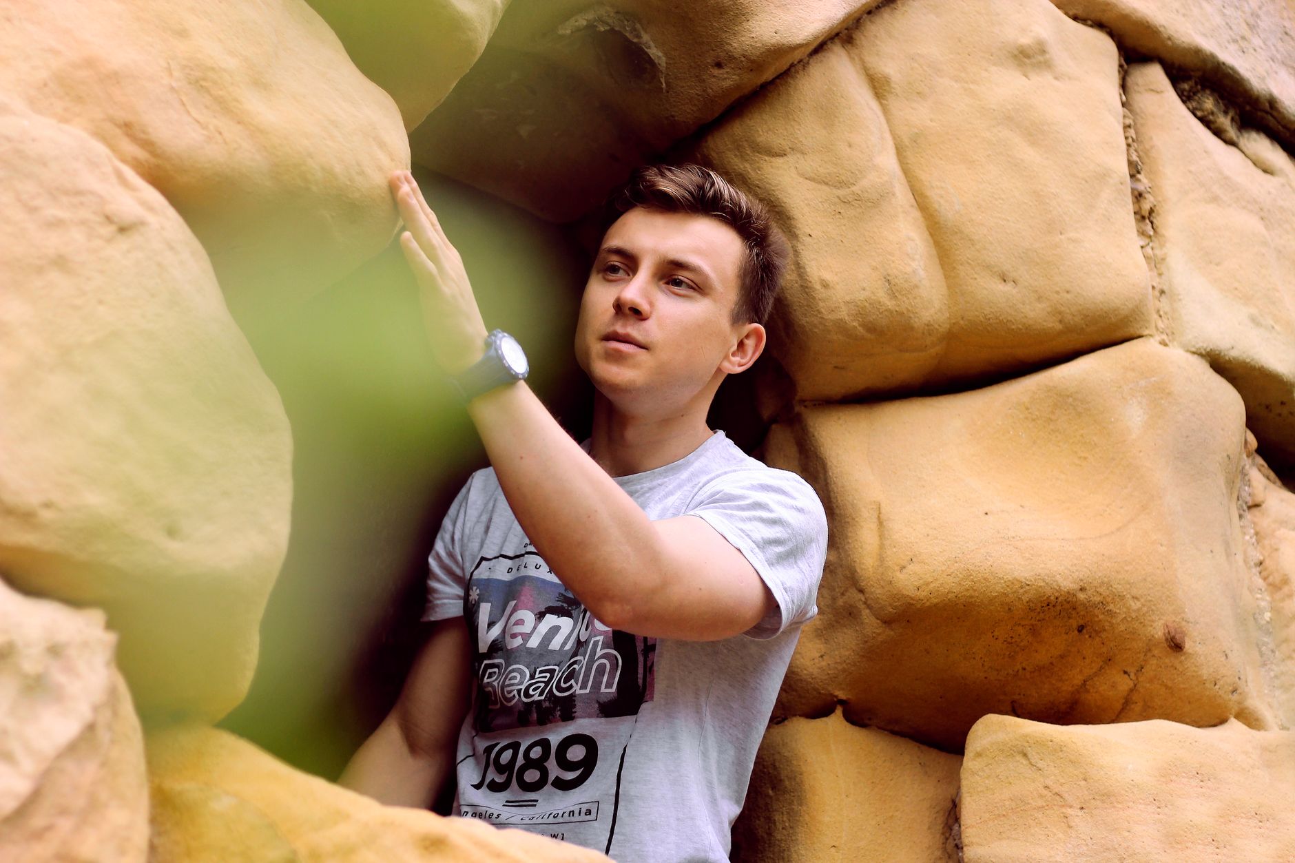 A young man exploring and touching a unique rock formation outdoors in daylight.