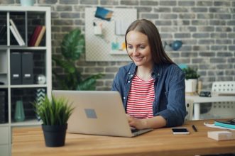 A woman uses a laptop at a stylish desk in a bright, modern office setting.
