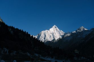 Majestic snow-covered Siguniang Mountain peak against a clear blue sky in a serene landscape.