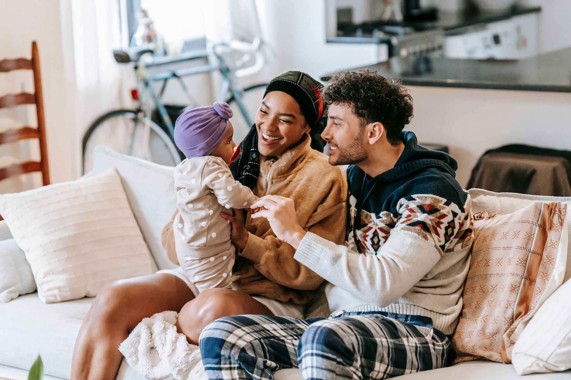 Positive black mother and father interacting with cute toddler child in headscarf while sitting on couch at home