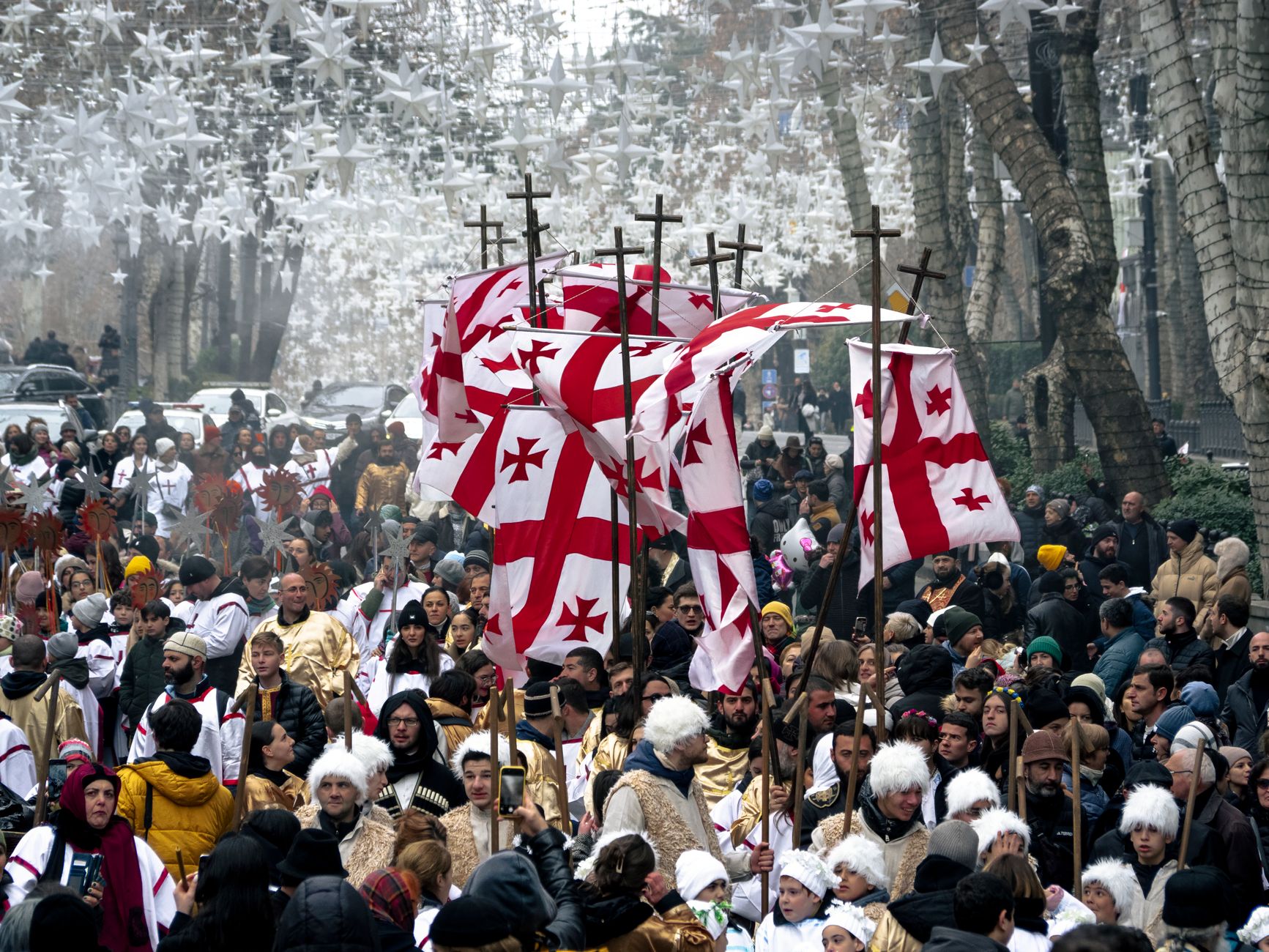 Festive crowd in a traditional Georgian parade displaying flags and cultural attire.